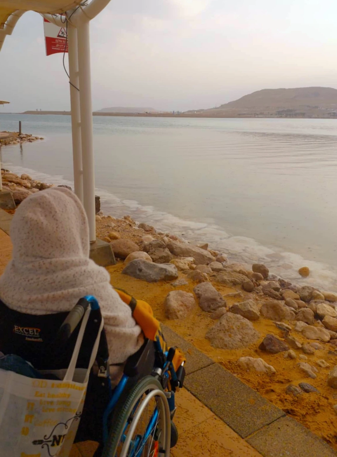 Ester Rot, the elderly woman with whom Monica Biboso works as a caregiver, on the shore of the Dead Sea. After surviving the massacre carried out by Hamas on Oct. 7, 2023, the two were displaced to the David Dead Sea Resort along with the other surviving residents of Kibbutz Be'eri. Credit: Photo courtesy of Monica Biboso