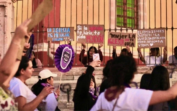 Catholic women inside the fencing around a church hold signs with messages such as “If the Church has hurt you, I ask forgiveness” and “Feminism is justice and justice begins with the right to life” during the International Women’s Day march on March 8, 2025, in Mexico. Credit: Magui Lozano