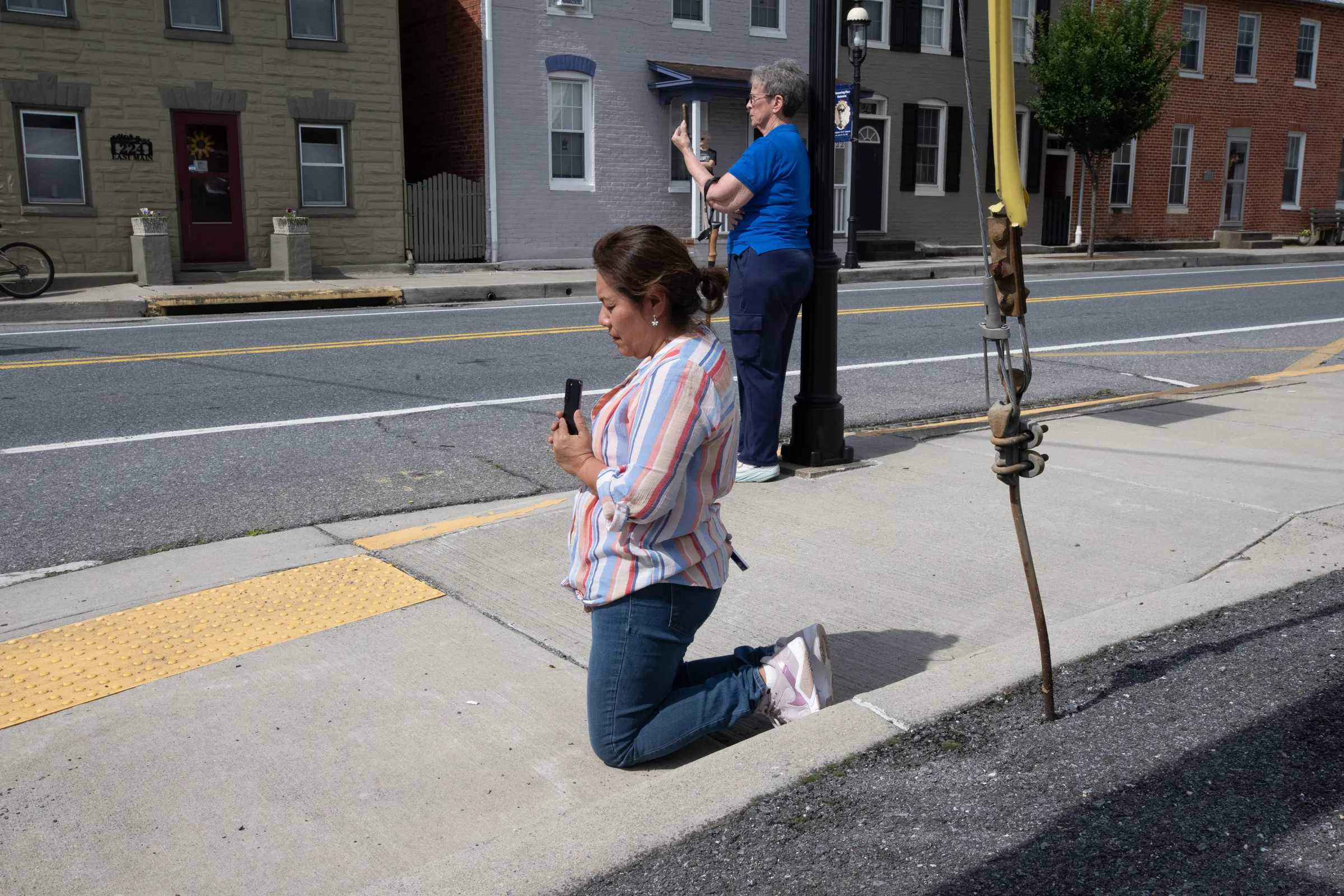 A woman kneels as the Eucharistic procession passes by. Credit: Jeffrey Bruno