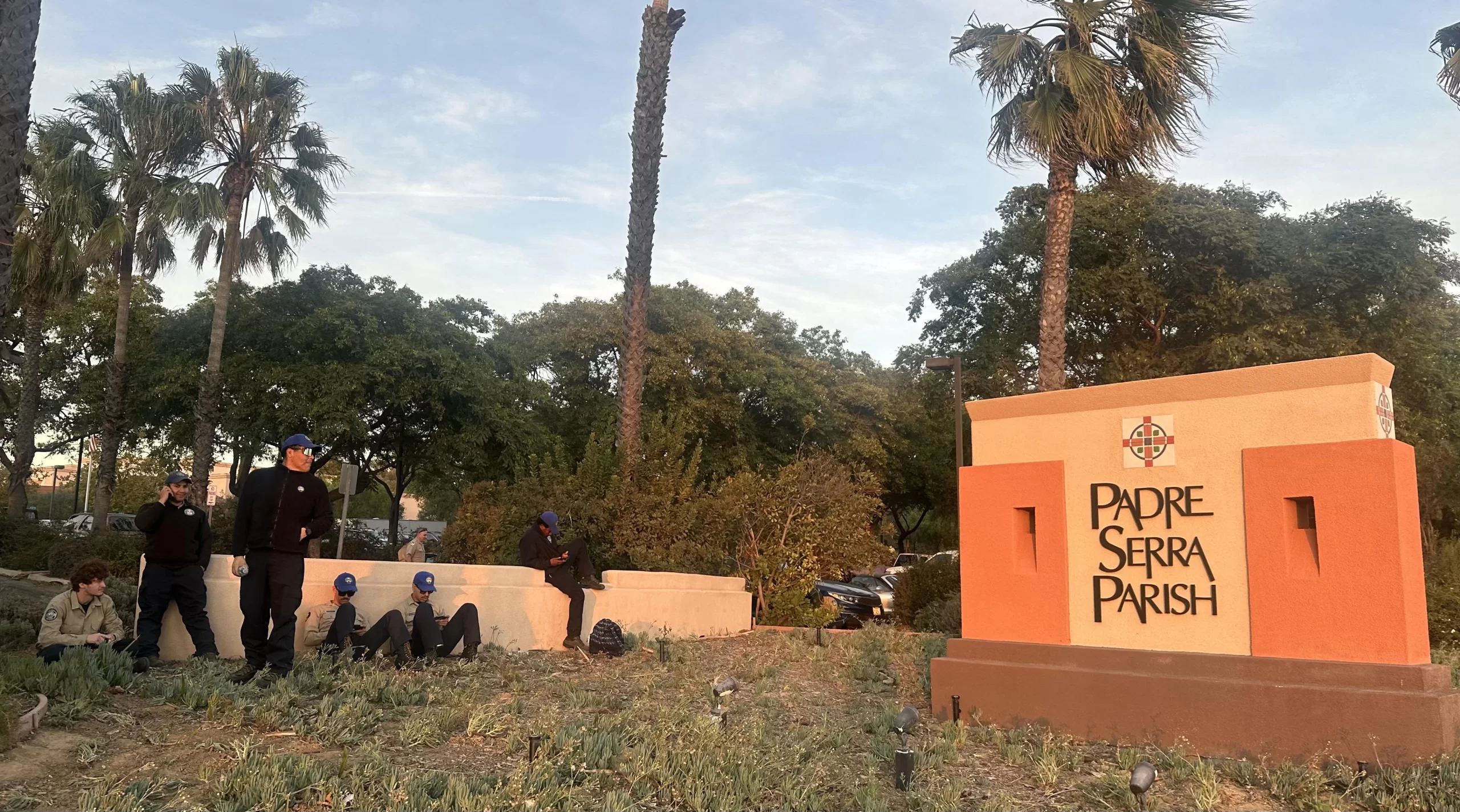 California Conservation Corp workers rest near the sign for Padre Serra Parish, which served as an evacuation center during the November 2024 Mountain Fire. Credit: Courtesy of Melissa Pettit