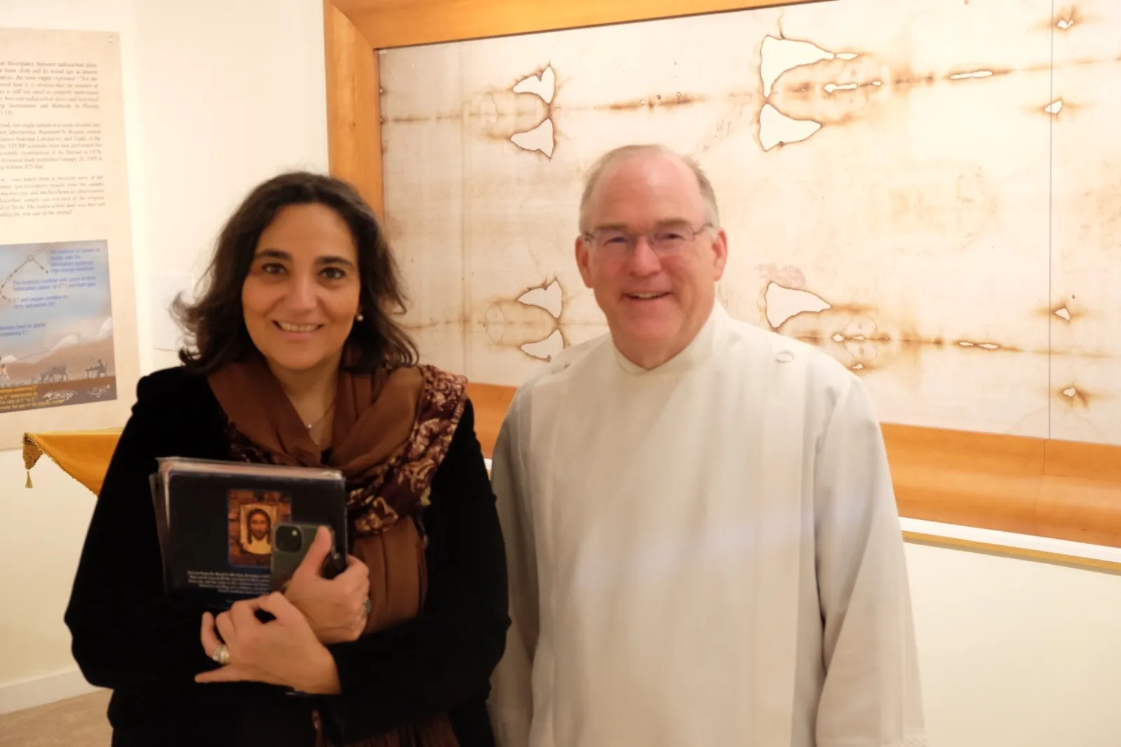 Father Bill Asbaugh, pastor of St. Thomas the Apostle Parish in Ann Arbor, Michigan, and Paola Conti-Puorger, custodian of the permanent exhibit, stand in front of a photographic reproduction of the Holy Shroud. Credit: Martin Barillas